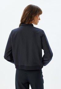 Navy jakke med lodrette hvide striber, ribbet krave og manchetter, afslappet pasform, struktureret stof og en cropped kant.