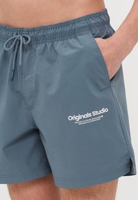 Shorts da bagno da uomo, grigi, in materiale leggero, vita elastica con coulisse, tasche laterali, con testo logo bianco sulla gamba sinistra.