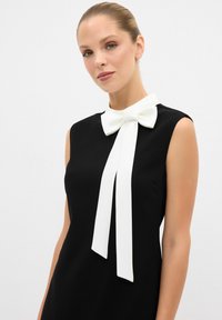 Schwarzes ärmelloses Kleid mit einer weißen Schleife am Ausschnitt, aus glattem Stoff mit einer schlanken Silhouette und ohne sichtbare Muster.
