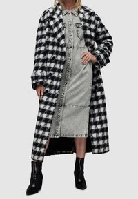 Musta-valkoinen ruutukuosisinen villakangastakki, pitkä ja suurilla napilla, kerroksittain harmaan farkkumekon päällä, jossa on napit edessä, sivuaukot ja mustat korolliset saappaat.