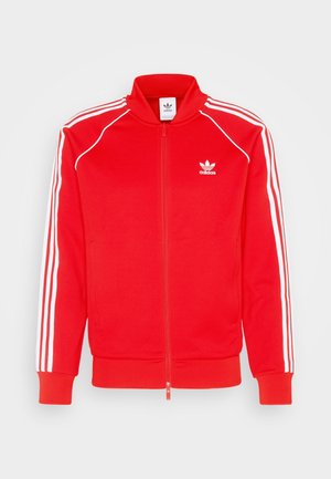 Rote Adidas-Trainingsjacke mit weißen drei Streifen an den Ärmeln, weißem Adidas-Logo auf der Brust, Frontreißverschluss und Seitentaschen.