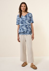 Top a maniche corte blu e bianco con scollo a V, abbinato a pantaloni beige chiaro a gamba larga e sandali marroni. Stile casual e vestibilità rilassata.