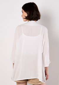 White lightweight blouse with a loose fit, featuring three-quarter sleeves, a round neckline, and delicate embroidered accents at the hem.