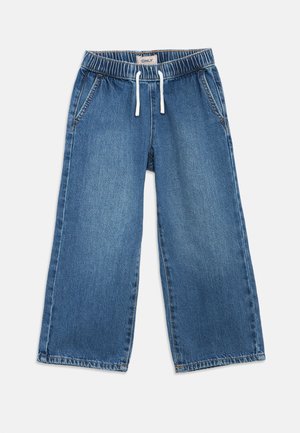 Calças largas de ganga azul com cintura elástica, fecho com cordão e dois bolsos laterais. O tecido tem uma textura suave com manchas desbotadas.