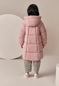 Puffet lyserød jakke med hætte, der har en quiltet design. Sammen med leopardmønstret bukser og hvide sneakers med lyserøde detaljer.