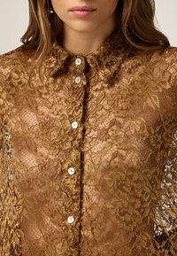 Lace blouse in golden brown with floral pattern, featuring a button-up front, collar, and semi-transparent texture.