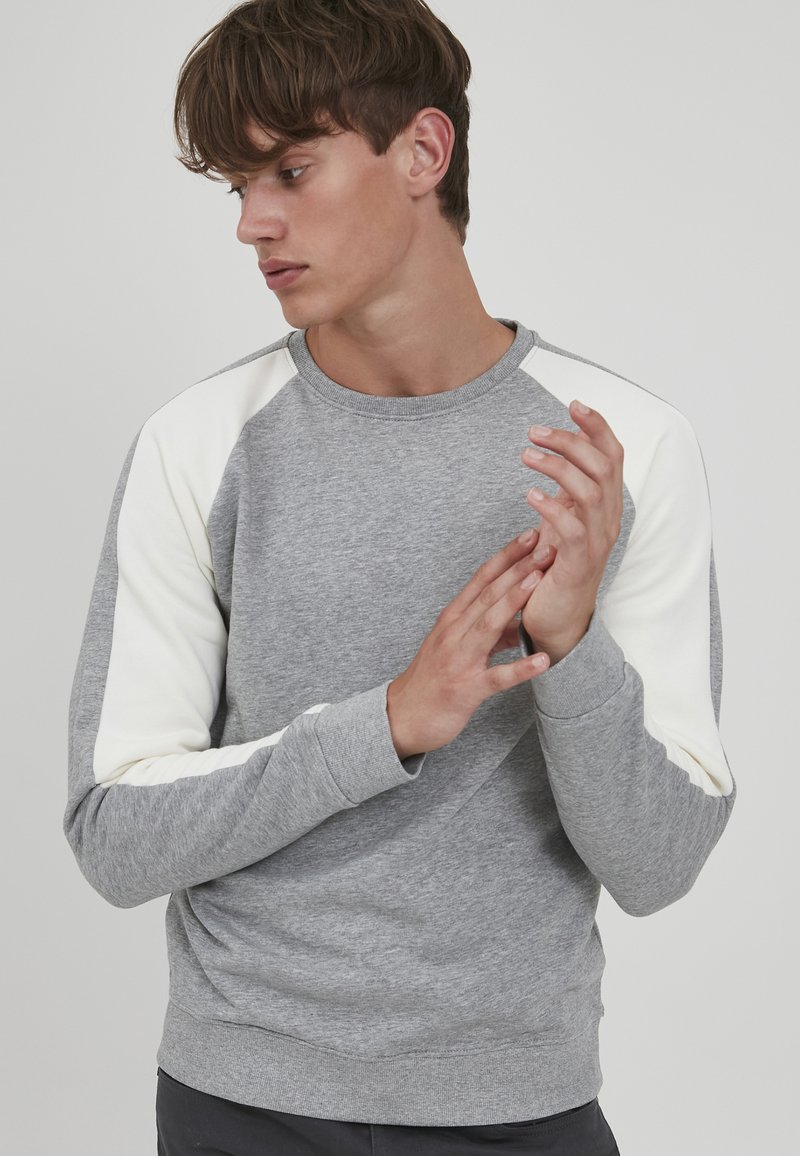 Grå sweatshirt med cremefarvede raglanærmer. Har en rund halsudskæring, ribbede manchetter og en glat tekstur. Simpelt design uden mønstre.