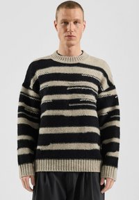 Pasiasty wełniany sweter z czarnymi i beżowymi poziomymi liniami, ściągaczem na dekolcie i mankietach oraz luźnym krojem z teksturowanymi detalami.