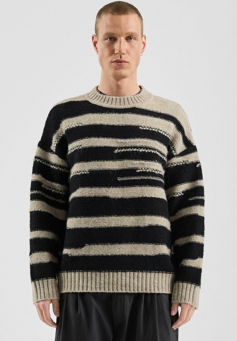 Pasiasty wełniany sweter z czarnymi i beżowymi poziomymi liniami, ściągaczem na dekolcie i mankietach oraz luźnym krojem z teksturowanymi detalami.