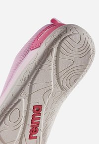Semelle de chaussure pour enfant rose et blanche inclinée vers le haut, montrant un motif de crampons texturés détaillé et le logo rouge « reima » au bas.
