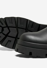 Stivaletto nero alla caviglia con punta arrotondata, tomaia in sintetico testurizzato e suola in gomma spessa e robusta con scanalature profonde per una buona trazione.
