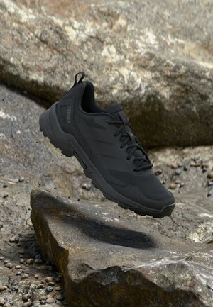 Scarpa outdoor nera con parte superiore strutturata, pannelli in mesh e suola in gomma. Presenta un marchio ben visibile, lacci e un tallone modellato.