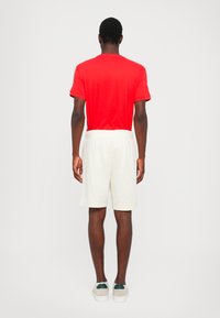 Rød bomull T-skjorte og hvite shorts, bakfra. Shortsene har en elastisk midje. Enkelt design uten synlige mønstre eller aksenter.