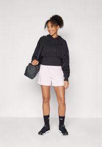 Črna skrajšana hoodie s vrvicami, svetlo roza kratke hlače, črne nogavice do gležnjev in črne športne čevlje. Nosite črno torbo.