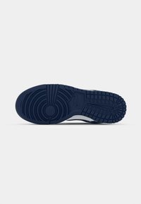 Navy rubber sneaker sole featuring circular and linear tread patterns, with a textured finish and a small, embossed logo.