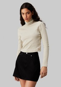 Heledbeez ribitatud turtleneck-särk pikkade varrukatega, koos musta denimpikk-särgi mini seeliku, millel on esiküljel taskud ja metallaktsendid.