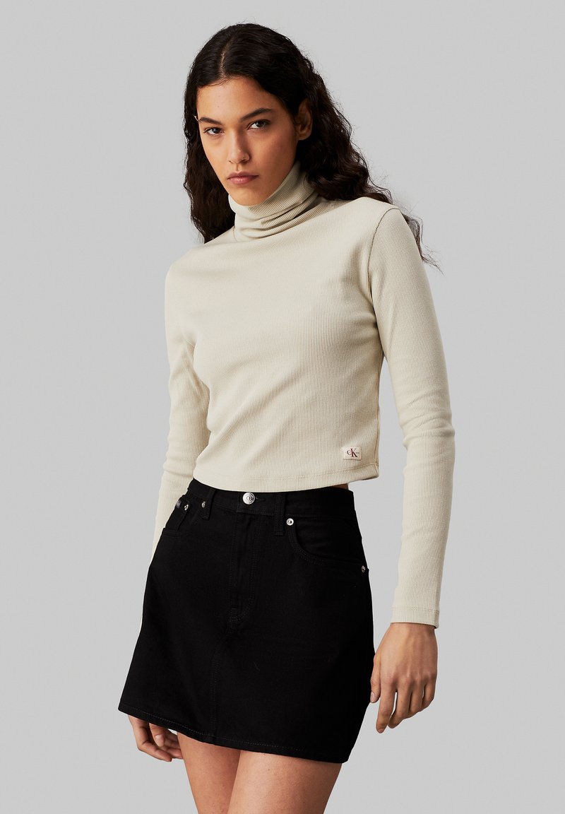 Heledbeez ribitatud turtleneck-särk pikkade varrukatega, koos musta denimpikk-särgi mini seeliku, millel on esiküljel taskud ja metallaktsendid.