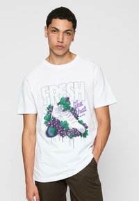 Hvit bomulls t-skjorte med grafisk trykk av sko omgitt av lilla druer og grønne blader, med teksten "FRESH like that."