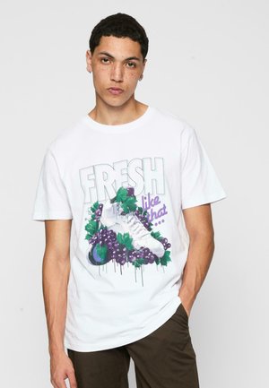 Hvid bomulds t-shirt med et grafisk print af sko omgivet af lilla druer og grønne blade, med tekst der står "FRESH like that."