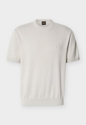 Kurzärmeliger beiger Pullover mit Rundhalsausschnitt, geripptem Saum und Bündchen, kleinem quadratischem Detail auf der linken Brust und gebrandetem Nackenlabel.