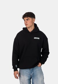 Felpa nera in cotone con tasca frontale. Presenta un logo bianco "CRYSTAL" sul petto e un logo geometrico sulla manica.