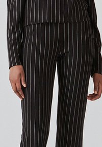 Sort stribet jakkesæt med en tætsiddende overdel og skræddersyede bukser, begge med lodrette striber og en glat tekstur.