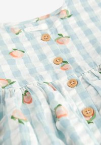 Robe à carreaux bleu clair et blanc avec des imprimés de pêches et des boutons en bois sur le devant.