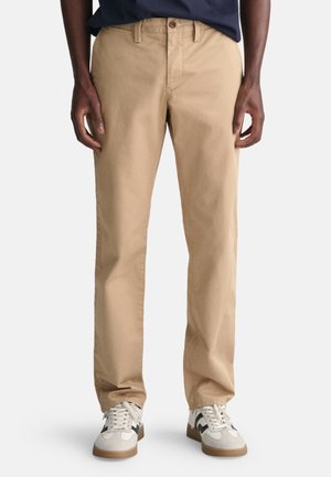 Beige cotton chinos with a straight fit, featuring a belt loop waist, front pockets, and flat front design, paired with white sneakers.