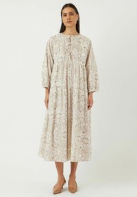 Lang, vloeiende jurk in crème met ingewikkelde beige bloemenpatronen, met een ronde halslijn, knopen detail en lange mouwen.
