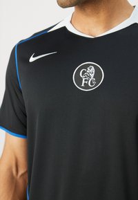 Sort fodboldtrøje lavet af letvægtsstof, med blå detaljer, en hvid krave og et rundt klublogo på fronten.