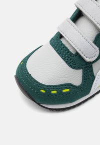 Basket verte et blanche avec une tige en cuir texturé et en daim, des sangles Velcro, des coutures contrastantes et des accents jaunes vifs.