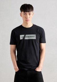 Black cotton t-shirt featuring a grey striped rectangular graphic with the text "ANONYMOUS" in bold letters across the front.