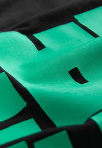 Tricou negru cu un grafic texturat verde, ce include forme geometrice și accente negre îndrăznețe. Material moale, cu o finisare netedă.