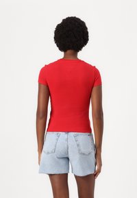 Rød tettsittende T-skjorte med korte ermer, glatt tekstur, rund halslinning. Båret med lyseblå høyhårede denimshorts med frynset kant.