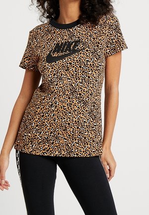 Mujer con una camiseta de manga corta de Nike con estampado de leopardo y logo negro, y leggings negros con franjas blancas en los laterales.