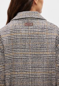 Παλτό μείγμα μαλλιού που διαθέτει σχέδιο καρό σε ναυτικό, κρέμ και μπεζ χρώματα, με λογότυπο στην πίσω πλευρά του γιακά. Διαθέτει κυματιστές πέτες και δομημένη εφαρμογή.