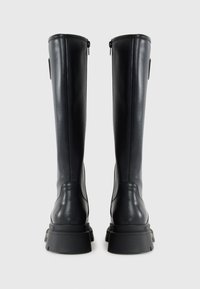 Botas negras hasta la rodilla hechas de cuero suave con una suela gruesa. Presentan cremalleras en la parte trasera y un diseño minimalista.