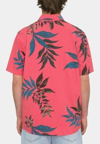 Camisa de manga corta en rosa brillante con estampado de hojas tropicales en azul y marrón oscuro. Tejido ligero, cuello abotonado, ajuste relajado.