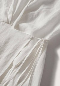 Tissu blanc avec couture froncée et fines attaches créant un détail cintré sous une lumière naturelle douce.