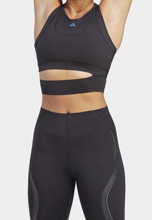 Czarny sportowy crop top z wycięciami i kontrastowym niebieskim logo; zestawiony z pasującymi, wysokimi legginsami z eleganckimi, zaokrąglonymi akcentami.