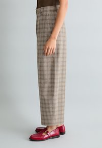 Braune karierte Hose mit weitem Schnitt, Falten und hoher Taille; kombiniert mit glänzenden roten Lederschuhen mit Schnallendetail.