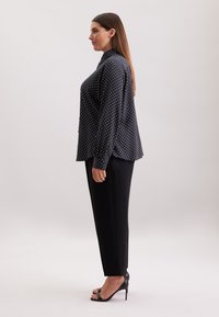 Zwarte blouse met stippen, hoog verwisselbare kraag, lange mouwen en een ontspannen pasvorm, gecombineerd met zwarte op maat gemaakte broeken en hoge hakken sandaaltjes.