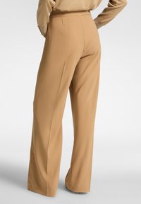 Breda byxor i tan-färg, tillverkade av ett mjukt tyg, med skräddarsydd passform, bakfickor och hög midja för en smickrande silhuett.