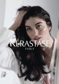 Affichage de produits Kérastase mettant en avant un modèle avec de longs cheveux foncés et brillants, portant un peignoir blanc, avec une surface réfléchissante en arrière-plan.