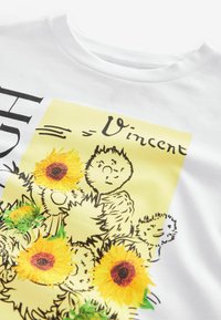 Vit bomull T-shirt med gul blommig grafik som föreställer solrosor och stiliserade figurer. Rund halsringning och mjukt material.