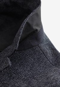 Abrigo texturizado de color azul oscuro con un cuello negro, que presenta un patrón tejido y detalles de tejido contrastantes. El material parece duradero.