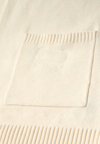 Texturovaná krémová tkanina se čtvercovou náprsní kapsou. Spodní část má žebrované detaily, které dodávají celkovému designu rozměr.