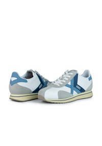 Zapatillas deportivas blancas y grises con acentos azules, que cuentan con un upper de ante y cuero, diseño de cordones y suela de goma.
