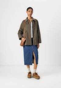 Olivově zelený kabát s zapínáním na knoflíky a velkým límcem, doplněný džínovou sukní s předním rozparkem a hnědými platformovými botami.