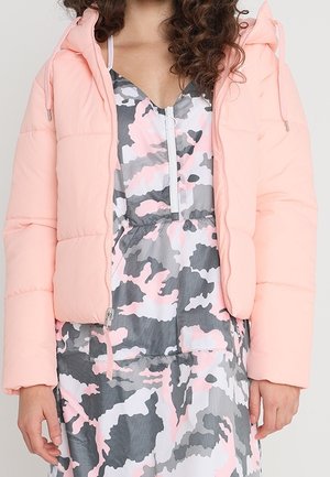 Gewatteerde korte jas in lichtroze met een capuchon, voorzien van een rits aan de voorkant en een koord. Daaronder een jurk in een grijs en roze camouflagepatroon.